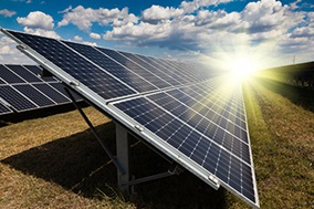 rows of solar panels on grass with sun rising behind