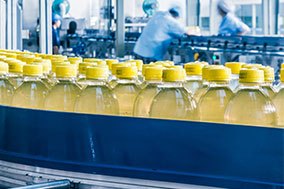 yellow beverage in plastic bottles on conveyor in factory with workers in background